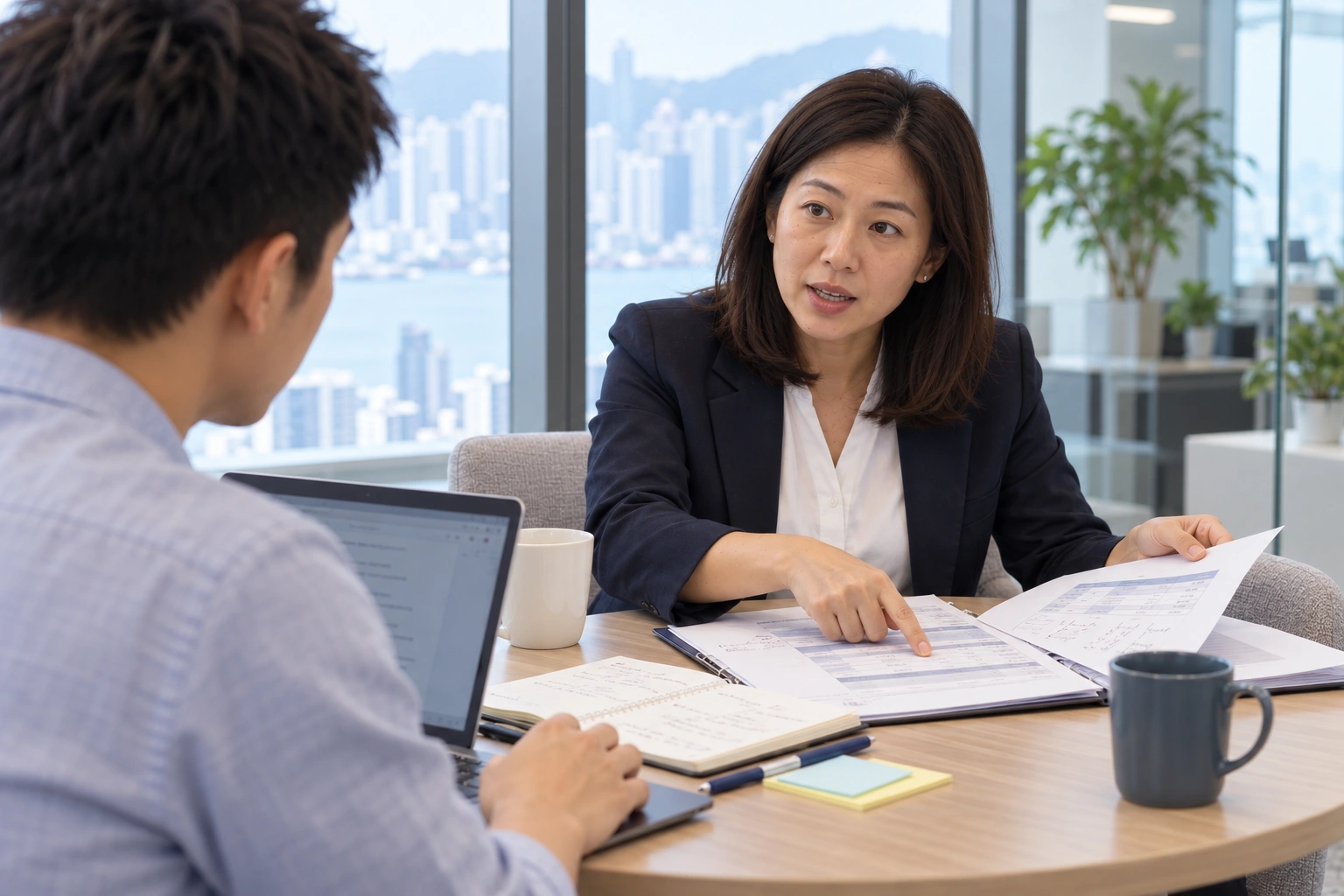 Illustrative service scene viewed from beside the engineer: the manager looks up while explaining her workflow across a round table with an open folder, annotated documents, and notes. The engineer listens with a laptop ready for recording key points.